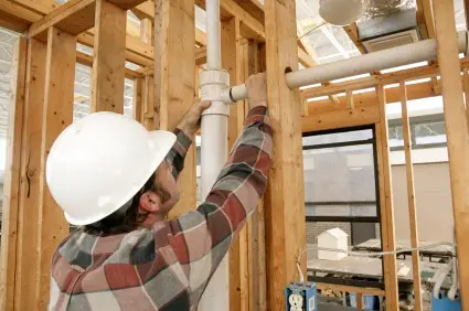 A construction worker connecting plumbing pipe in an unfinished wall. Focus is on the connecting pipes.